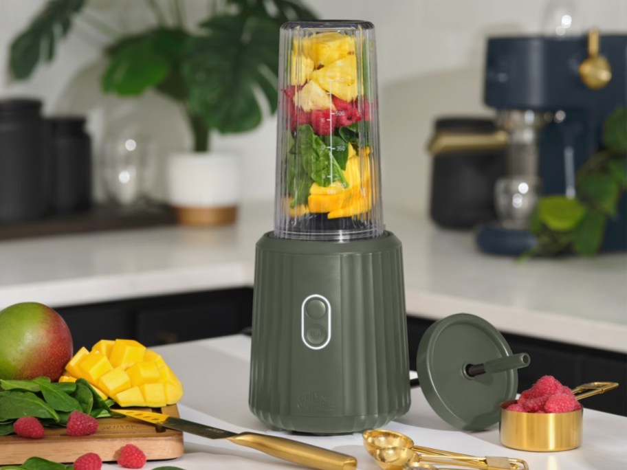 Thyme & Table Single Serve Blender in forest green sitting on kitchen counter with fruit inside ready to blend