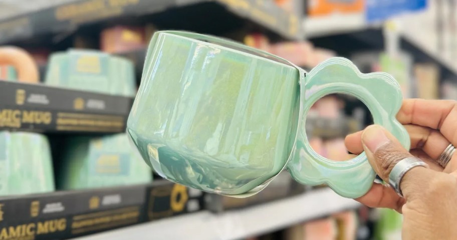 hand holding a green pearlescent coffee mug with a flower shaped handle