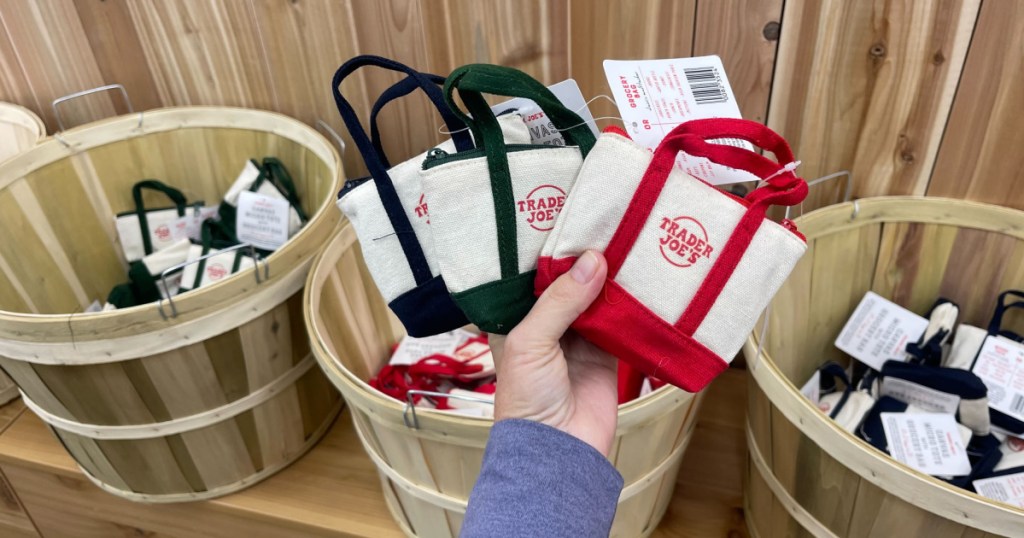 Woman holding up three different Trader Joe's, mini tote bags inside store