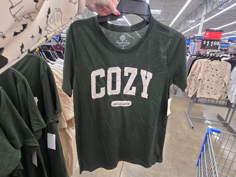 A person holding a gray t- shirt with the word "cozy" on it