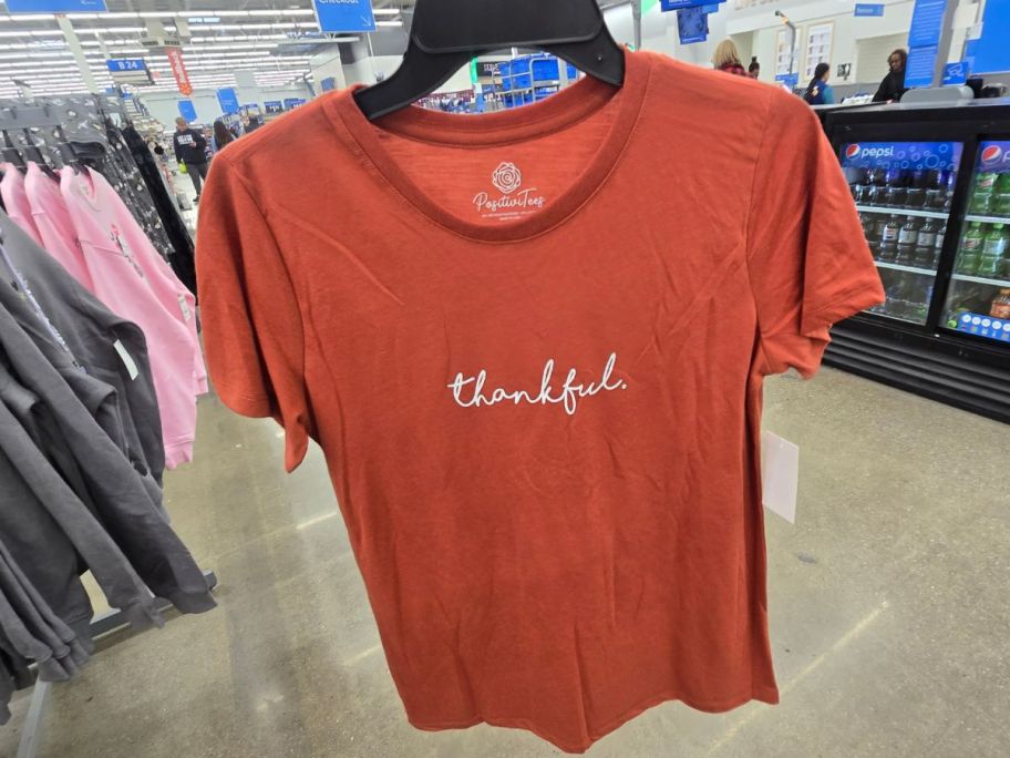 A person holding an orange t- shirt with the word "thankful" on it