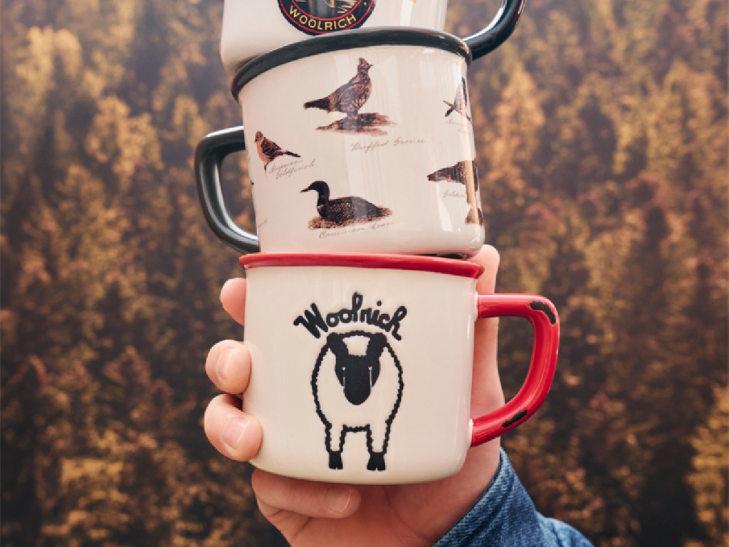 Man holding Woolrich coffee cups outside with trees in the background