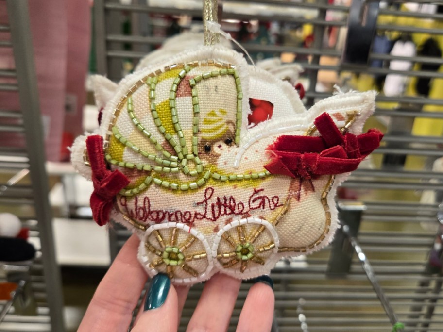 A hand hodling up a "welcome little one" baby buggie ornament.