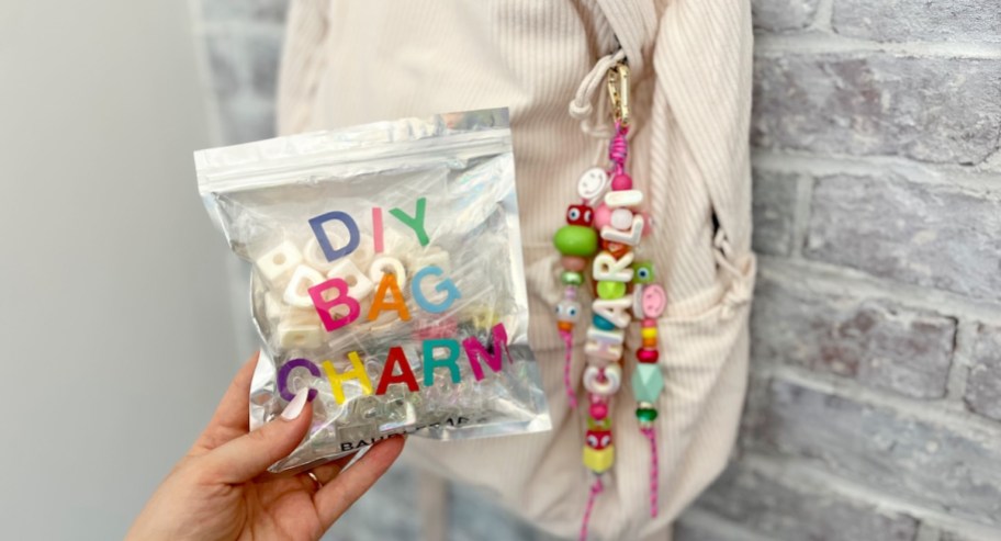 hand holding a diy bag charm bag with bookbag and keychain hanging on wall