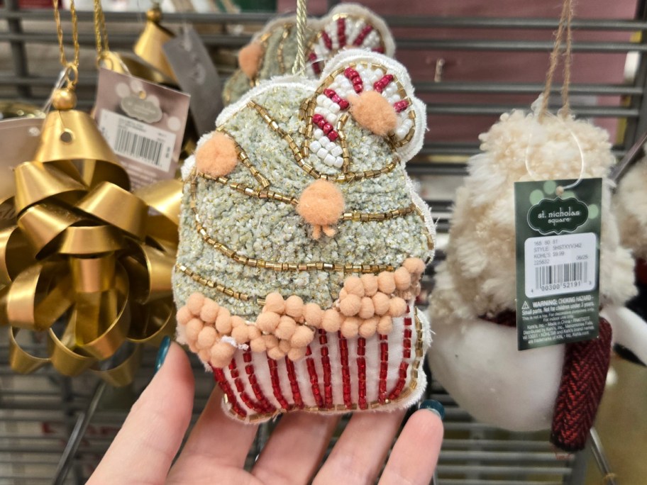 A hand holding up a beaded cupcake ornament.