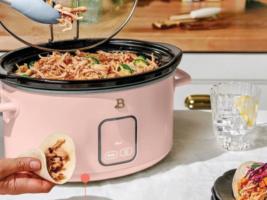 person lifting lid off pink slow cooker