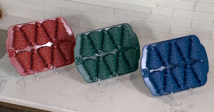 three christmas tree cakelet pans in red, green, and blue on counter