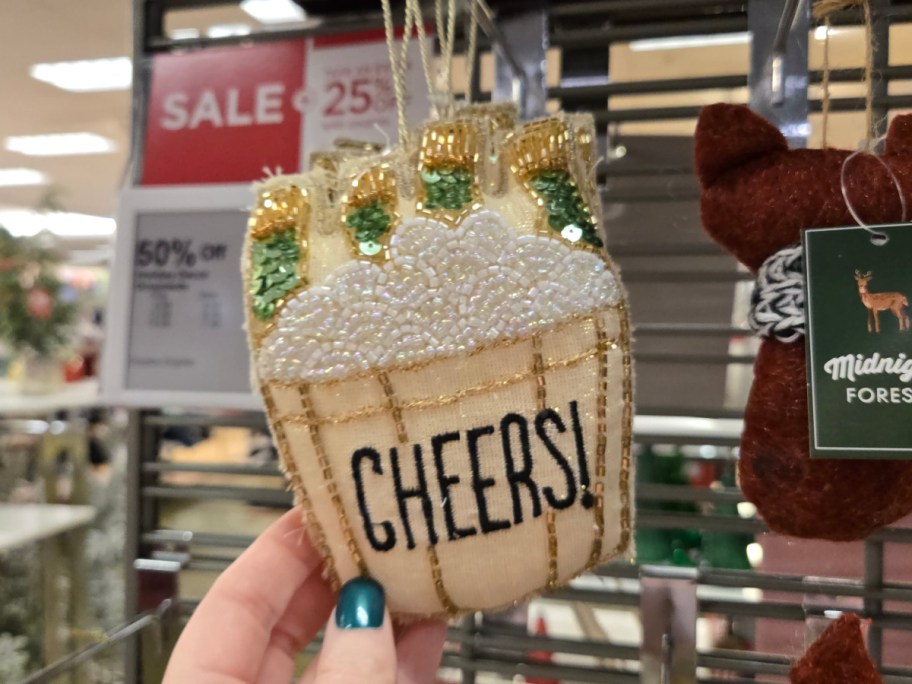 A hand holding up a cheers holiday bucket ornament.