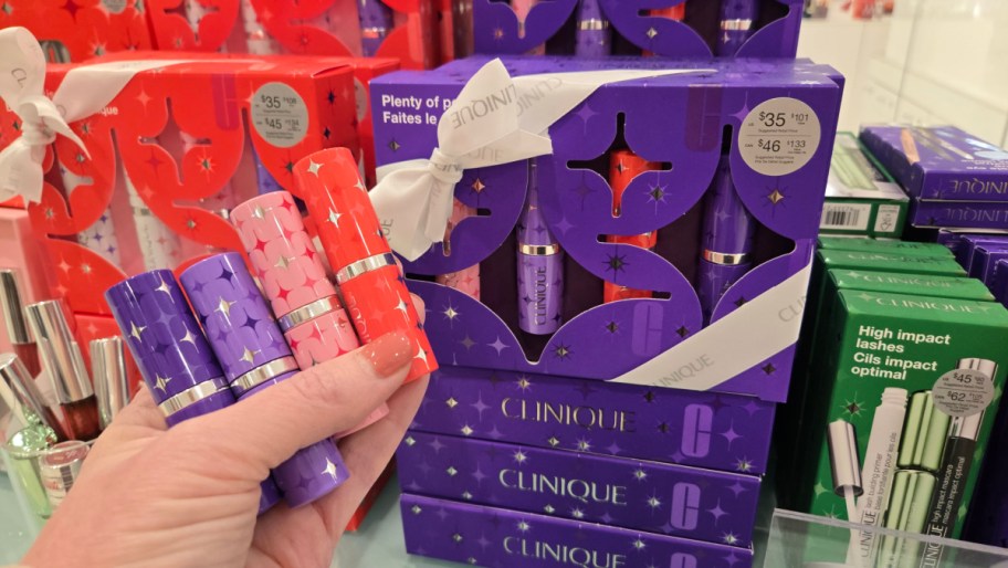 hand holding four lipsticks in front of a clinique gift set package