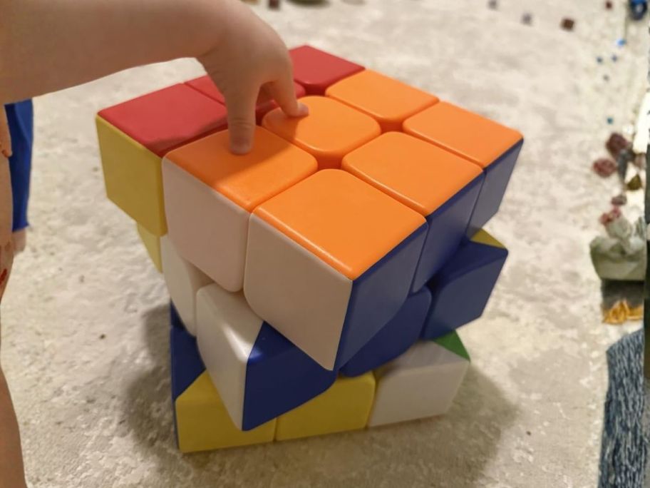 hand touching top of huge magic cube on floor