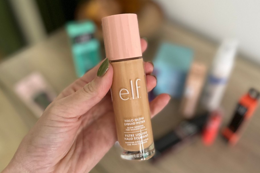 hand holding tube of glow concealer over other makeup products