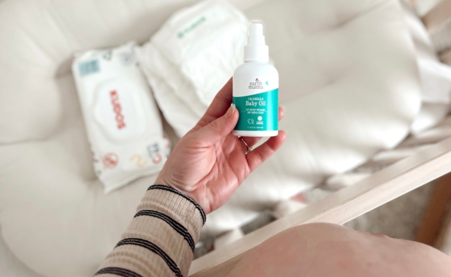 hand holding a bottle of baby oil over crib with wipes and diapers