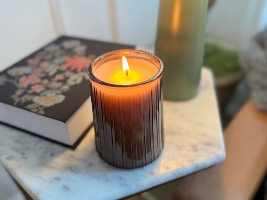 lit candle on an end table next to a book and lamp