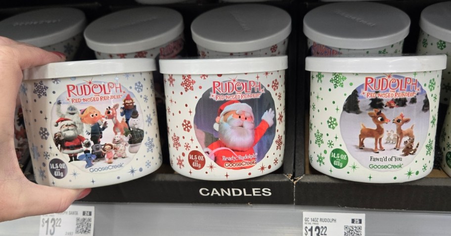 hand reaching for Rudolph the Red Nosed Reindeer themed Goose Creek Candles on a store shelf