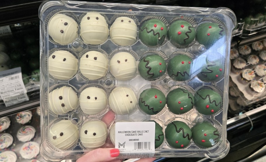 a womans hand holding a tray of halloween themed cake balls