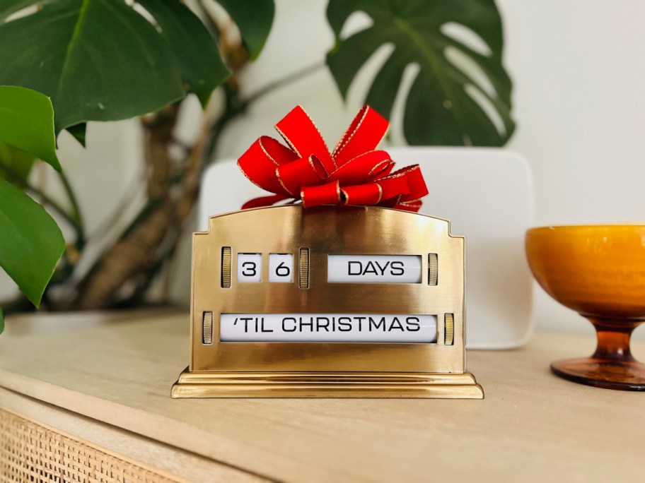 brass perpetual advent calendar with a red bow on it, on a desk