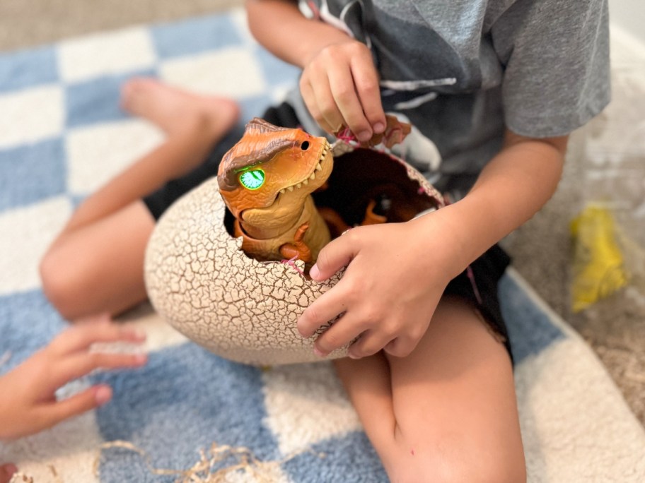 a little boy holding a dinosaur egg with a dinosaur hatching from it