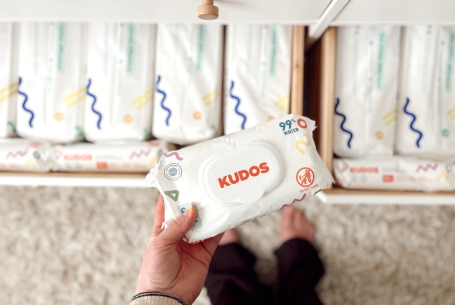 hand holding a pack of kudos baby wipes with open drawers full of diapers