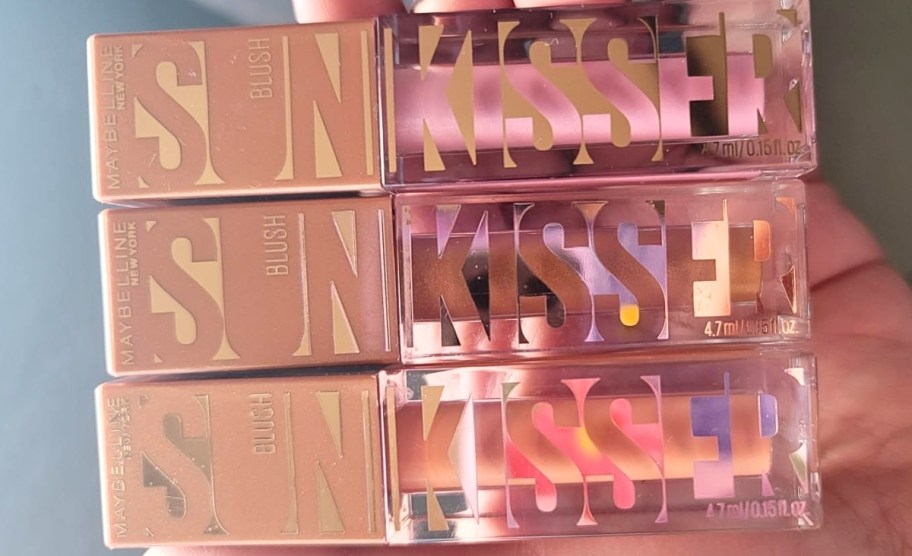 a womans hand holding 3 tubes of maybelline sunkisser blush 