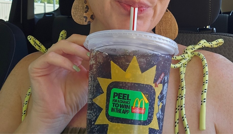 a woman sipping through a straw from amc donalds cup with a monopoly game piece on the side