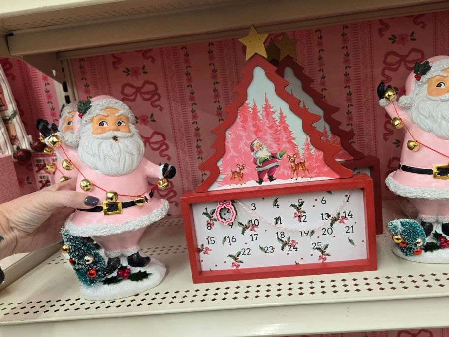 Pink Santa w/ Bells Tabletop Décor and Red & White Christmas Tree w/ Santa Countdown Tabletop Décor on shelf in store