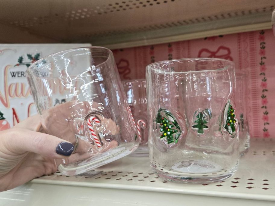hand holding Clear Glass with candy canes on it with a glass with christmas trees in next to it