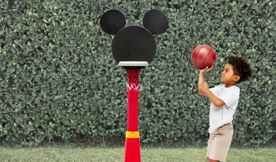 a little boy making a shot into the hoop of a mickey mouse basket ball set