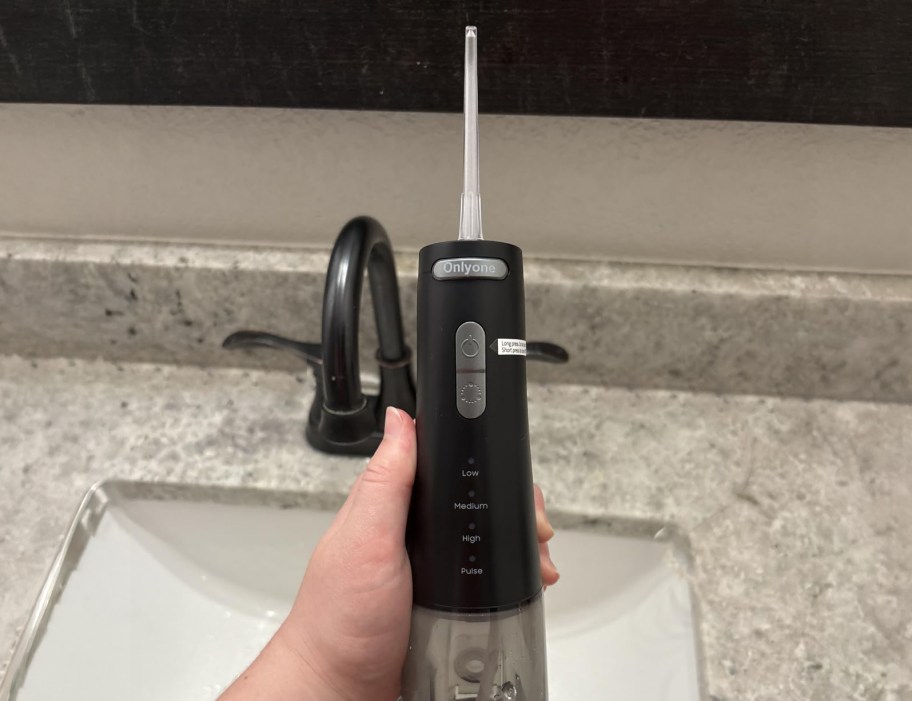 person holding water flosser by a sink