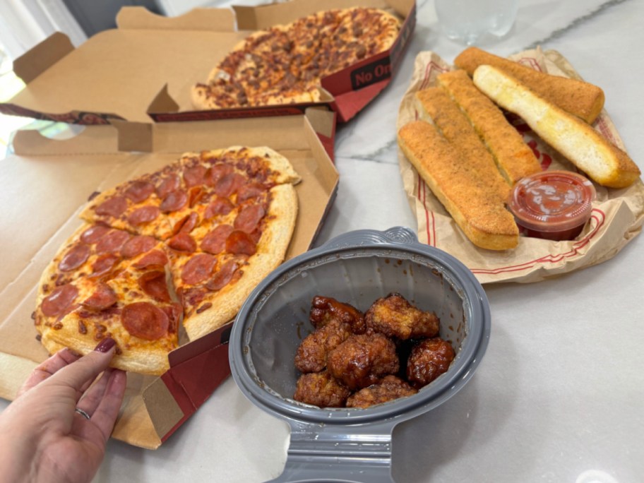 two pizza hut pizzas, wings, and breadsticks displayed on a countertop