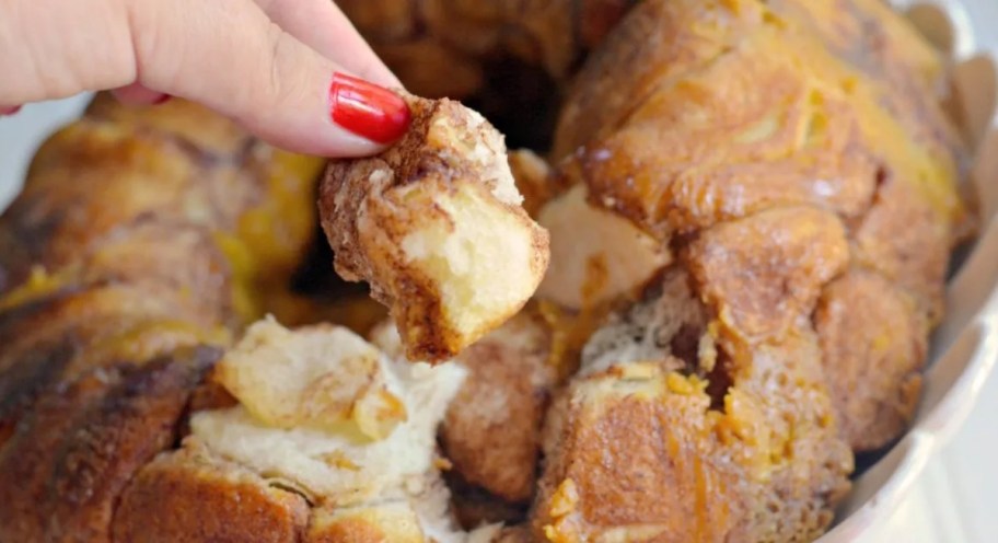 a woman grabbing a bite of PSL cheesecake monkey bread