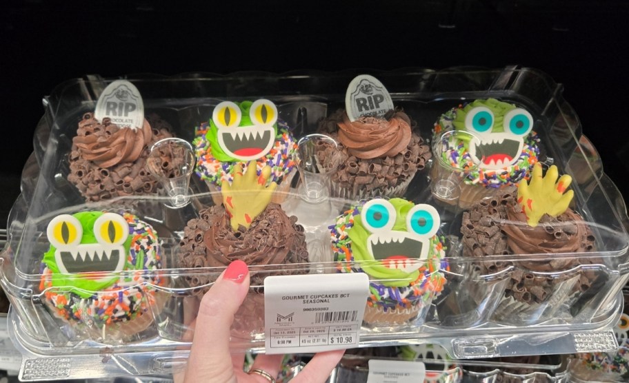 a womas hand holding a tray of halloween monster cup. cakes