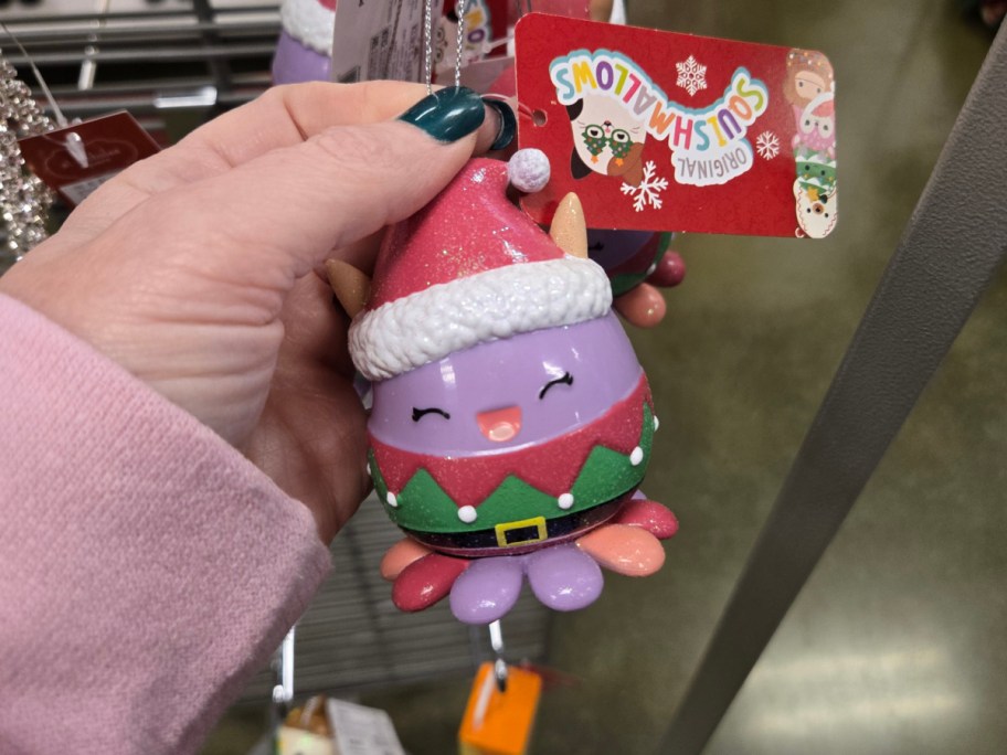 A hand holding up a Squishmallows oranament.