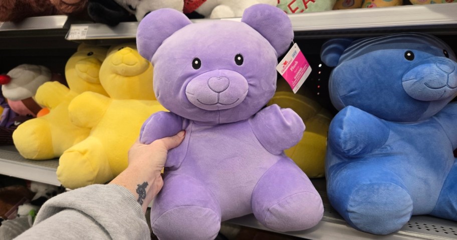 hand holding a large purple gummy bear plush with more colors on a store shelf behind it