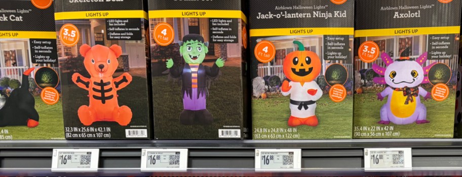 A store shelf of Way to Celebrate Halloween inflatable boxes featuring a skeleton bear, Frankenstein, a Jack-o'-lantern ninja kid, and an axolotl.