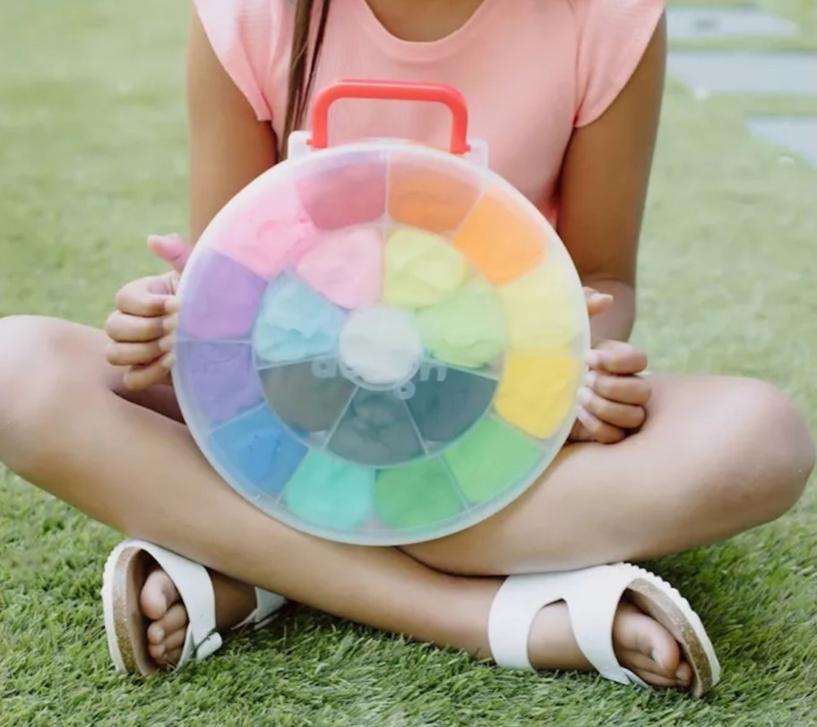 girl holding rainbow whoa dough kit in grass