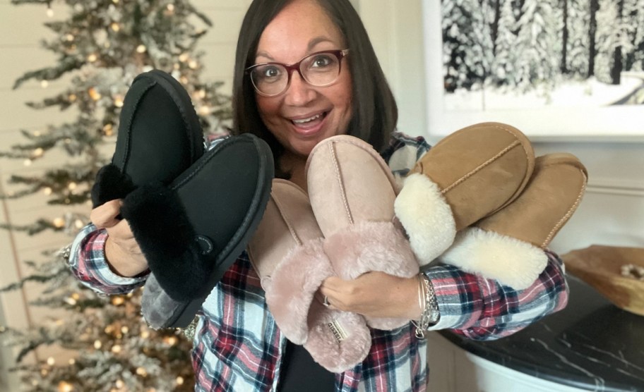 a woman holding 3 pair of dearfoams slippers