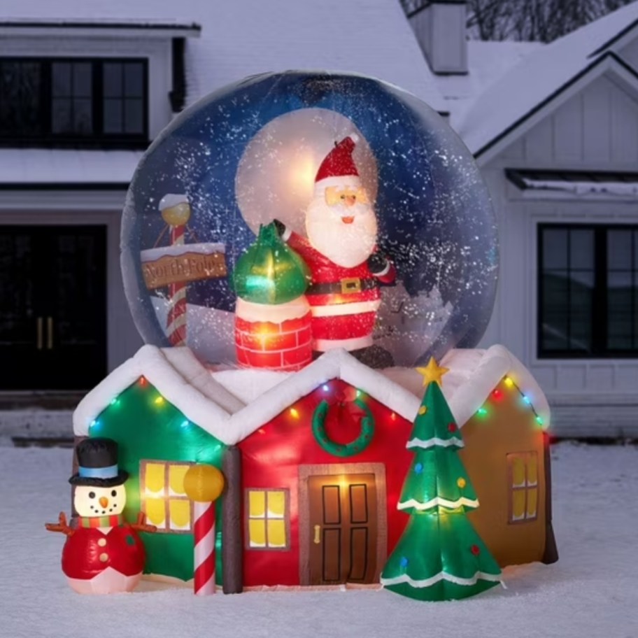a large inflatable snowglobe with Santa Christmas decor in a yard