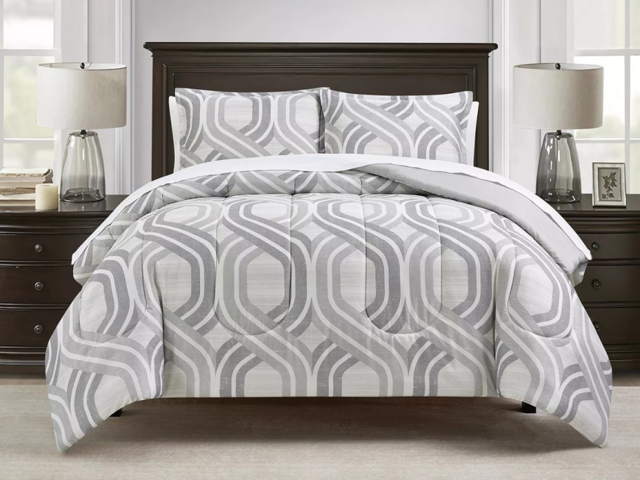 a bed with a white and grey geometric print comforter set on it
