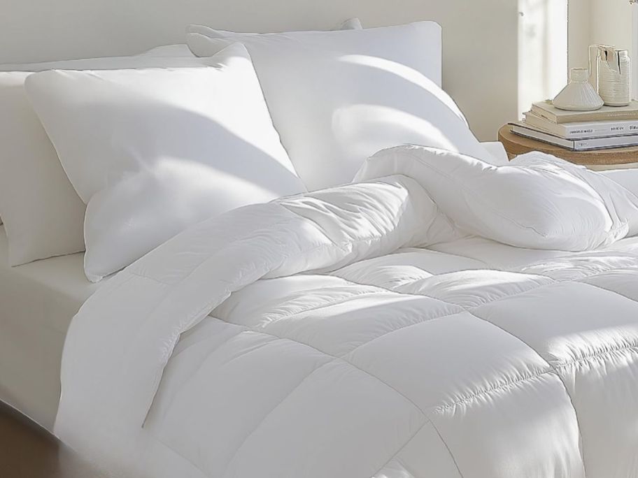 A bed with a white comforter and white pillows on it