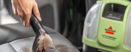 Hand using a Little Green Mini Portable Cleaner in the car