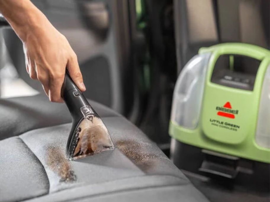 Hand using a Little Green Mini Portable Cleaner in the car