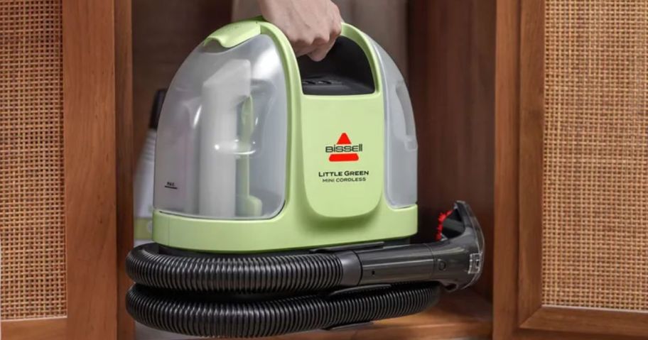 Hand putting a Little Green Mini Cordless Carpet Cleaner in a cabinet