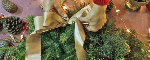 hand tying a gold bow onto a christmas wreath