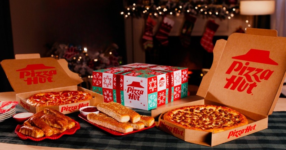 boxes with different Pizza Hut food items in them on a table with holiday decor behind it