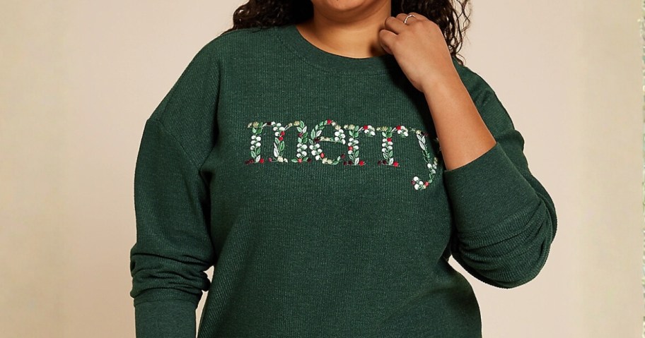 woman wearing a green sweatshirt that says "Merry" in floral lettering