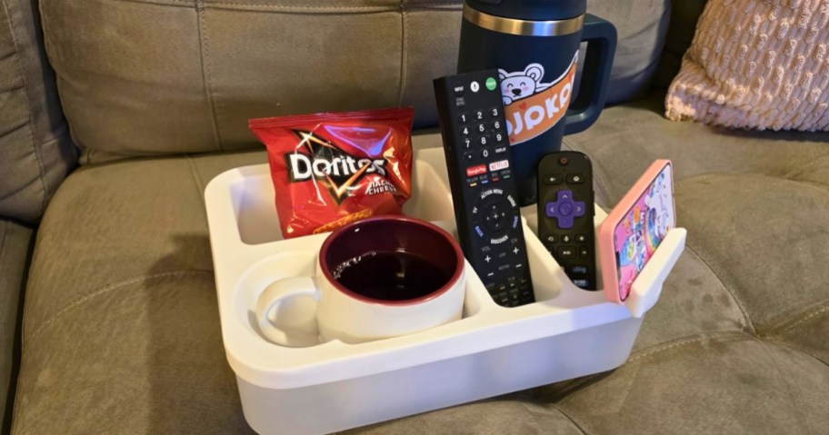 a white couch caddy with snacks and tumblers in it on a couch