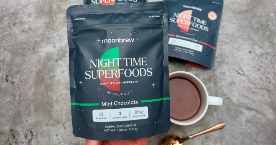 hand holding a bag of Moonbrew Nighttime Sleep Aid, mug with the mix and more bags behind it