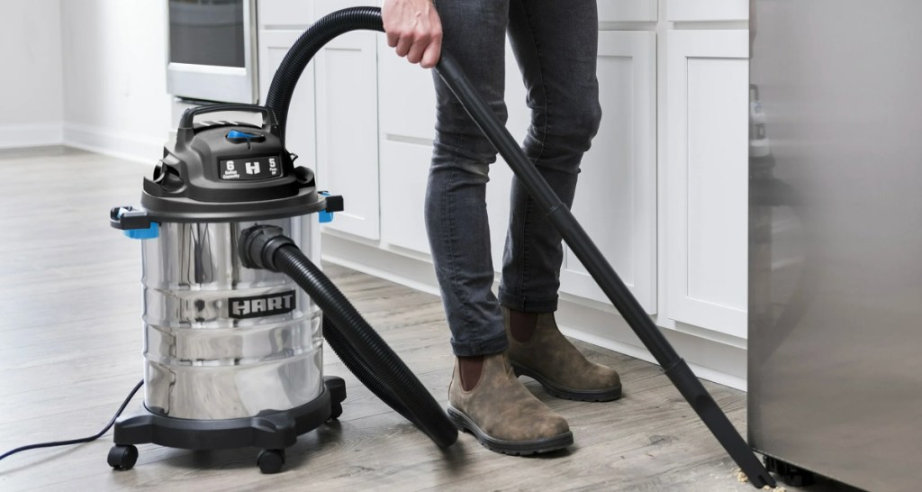 Man using stainless steel vacuum in kitchen to vacuum cereal underneath the refrigerator