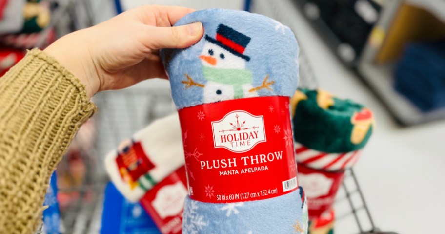 Woman holding up snowman themed holiday throw blanket inside Walmart store