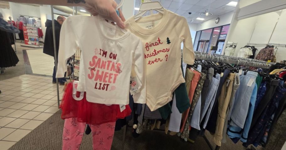 A person holding up baby clothing